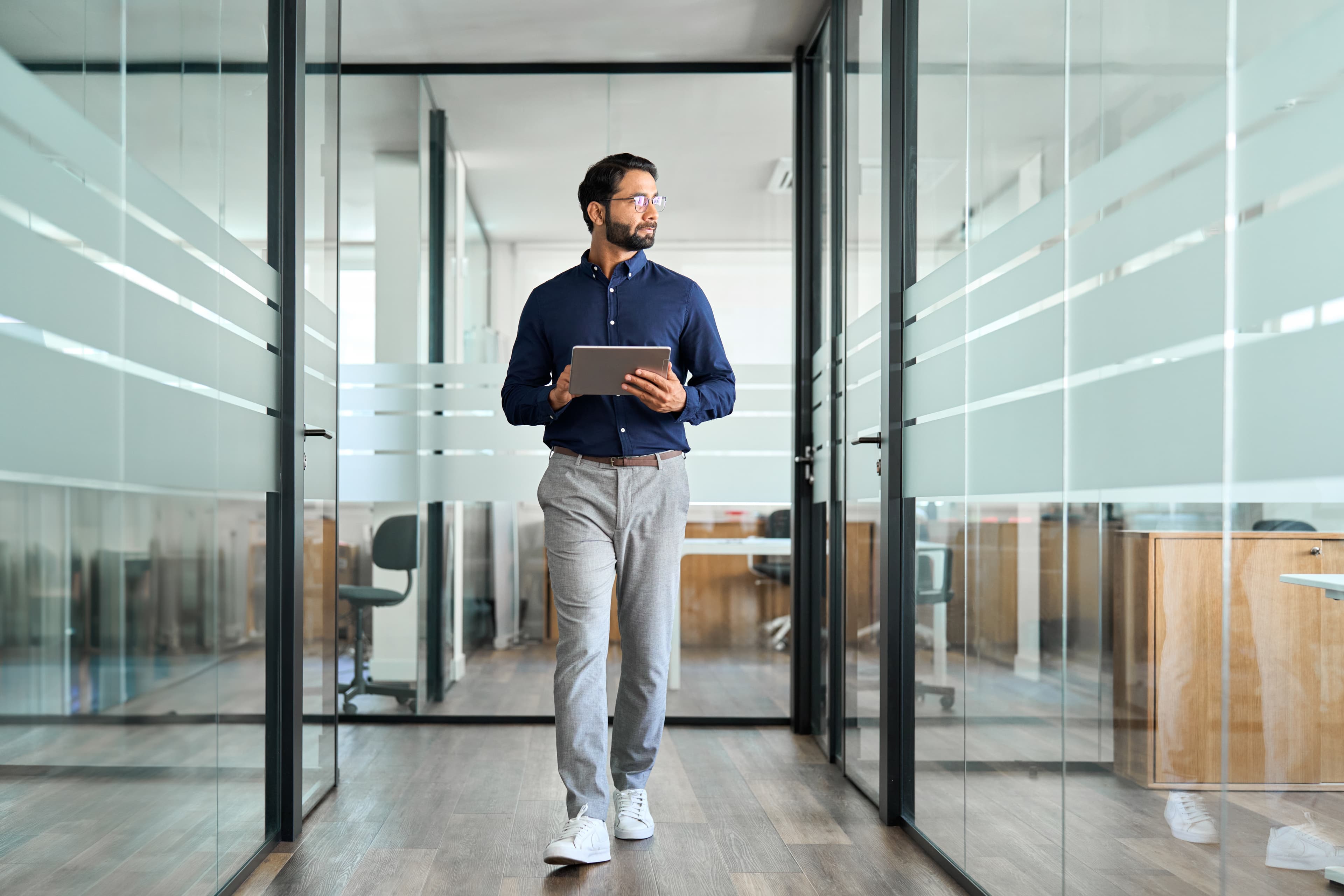 Business professional walking confidently through a modern glass corridor.