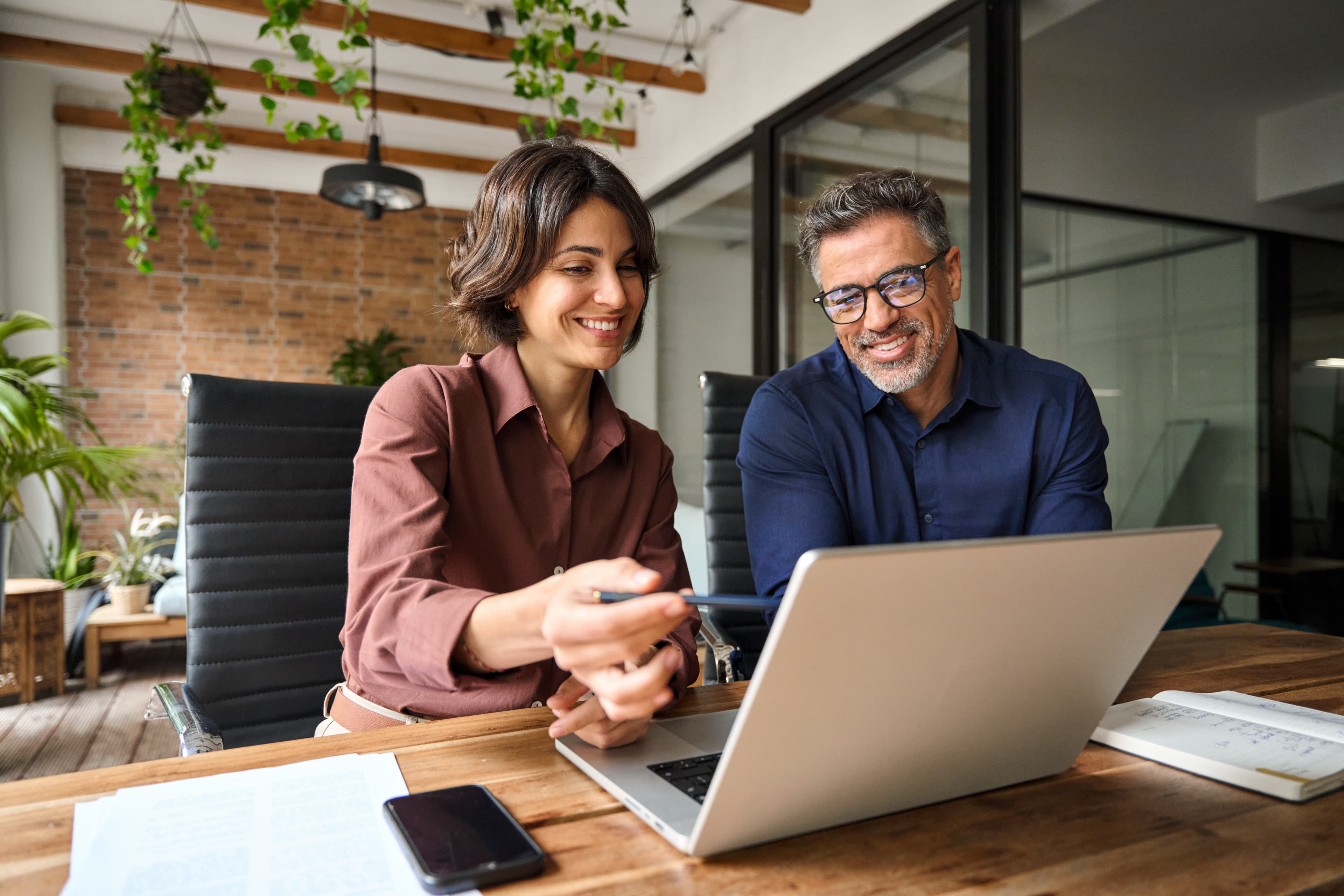 Two colleagues working together on a laptop in a casual office environment.